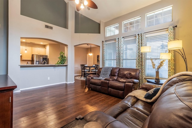 living area featuring a wealth of natural light, visible vents, arched walkways, and dark wood-style flooring