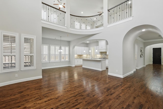 unfurnished living room with ceiling fan, arched walkways, recessed lighting, baseboards, and dark wood-style floors