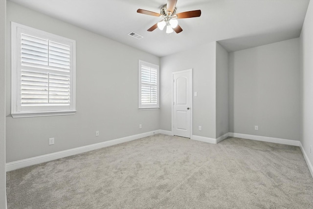 empty room featuring a ceiling fan, visible vents, light carpet, and baseboards