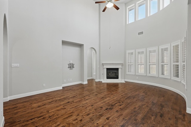 unfurnished living room with dark wood-style flooring, visible vents, a glass covered fireplace, ceiling fan, and baseboards