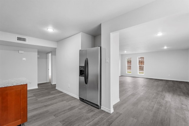 kitchen with light stone counters, visible vents, baseboards, stainless steel refrigerator with ice dispenser, and dark wood finished floors