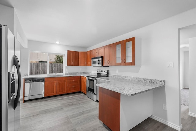 kitchen featuring brown cabinets, stainless steel appliances, glass insert cabinets, a sink, and a peninsula