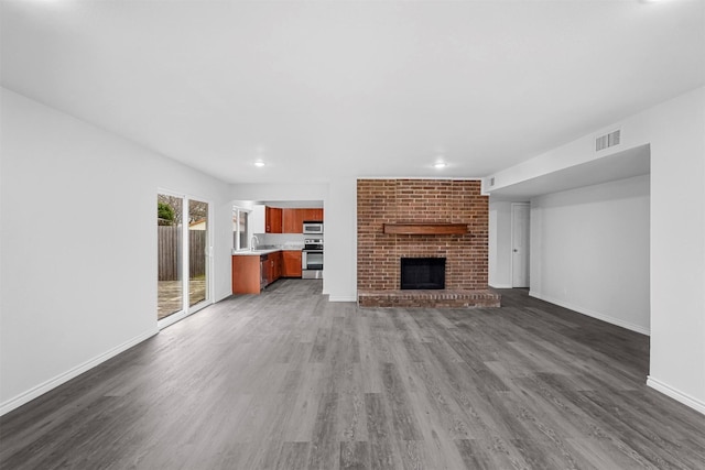 unfurnished living room featuring baseboards, visible vents, dark wood-style floors, a fireplace, and a sink