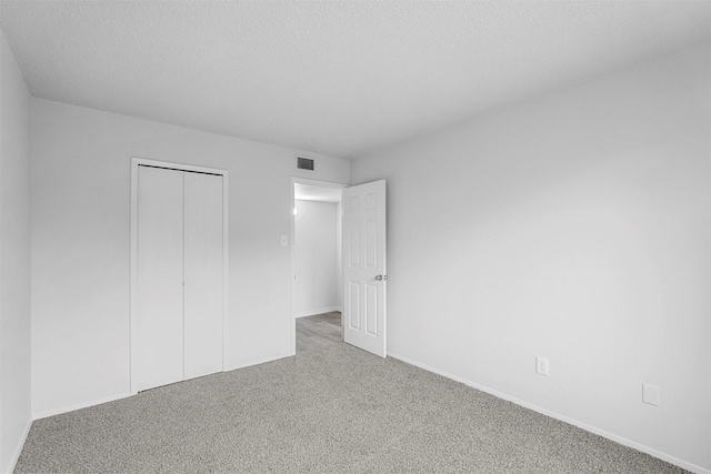 unfurnished bedroom with a closet, visible vents, carpet flooring, a textured ceiling, and baseboards