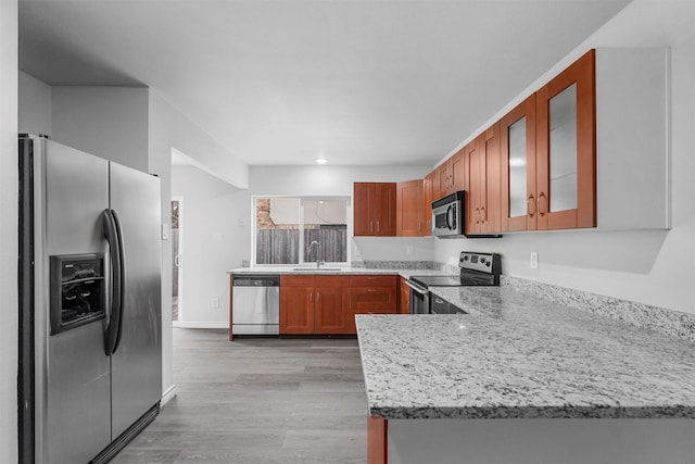 kitchen featuring light wood-style flooring, a peninsula, appliances with stainless steel finishes, brown cabinets, and glass insert cabinets