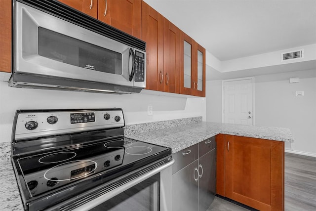 kitchen with visible vents, glass insert cabinets, appliances with stainless steel finishes, a peninsula, and light stone countertops