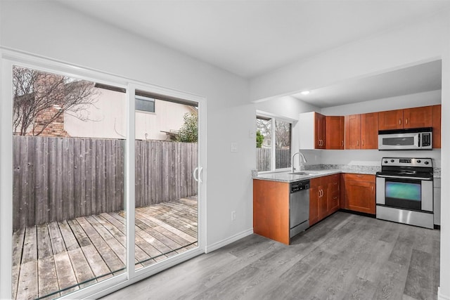 kitchen featuring baseboards, brown cabinets, stainless steel appliances, light wood-style floors, and a sink