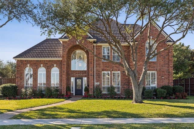 view of front facade with a front yard, brick siding, fence, and a tiled roof