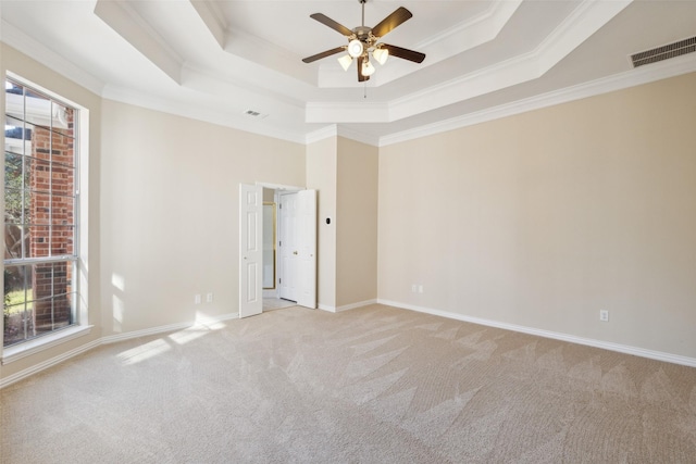 empty room featuring a tray ceiling, visible vents, ornamental molding, light carpet, and baseboards