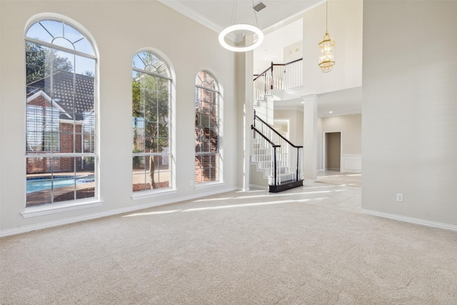 carpeted spare room with crown molding, a high ceiling, baseboards, stairway, and ornate columns