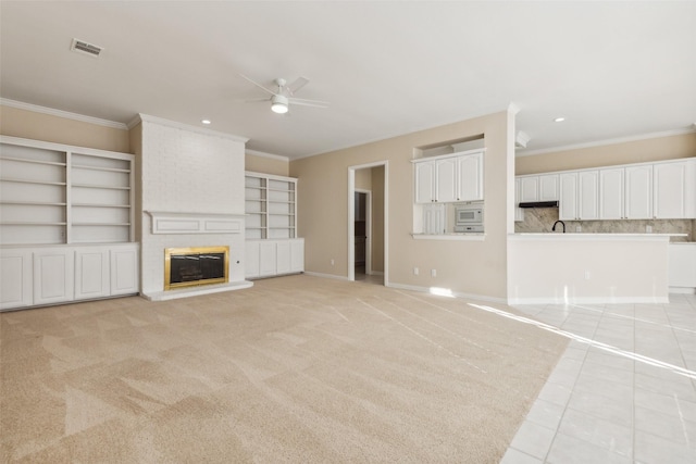 unfurnished living room featuring a ceiling fan, a brick fireplace, visible vents, and crown molding