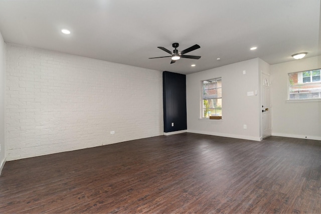 spare room featuring brick wall, dark wood-type flooring, and a wealth of natural light