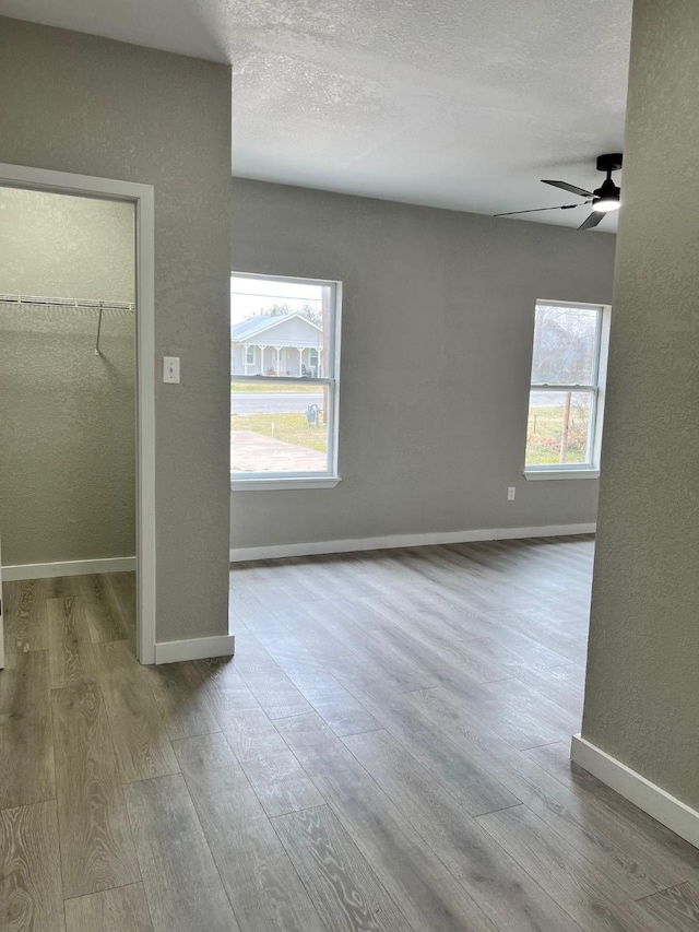 unfurnished bedroom featuring a spacious closet, a textured ceiling, baseboards, and wood finished floors