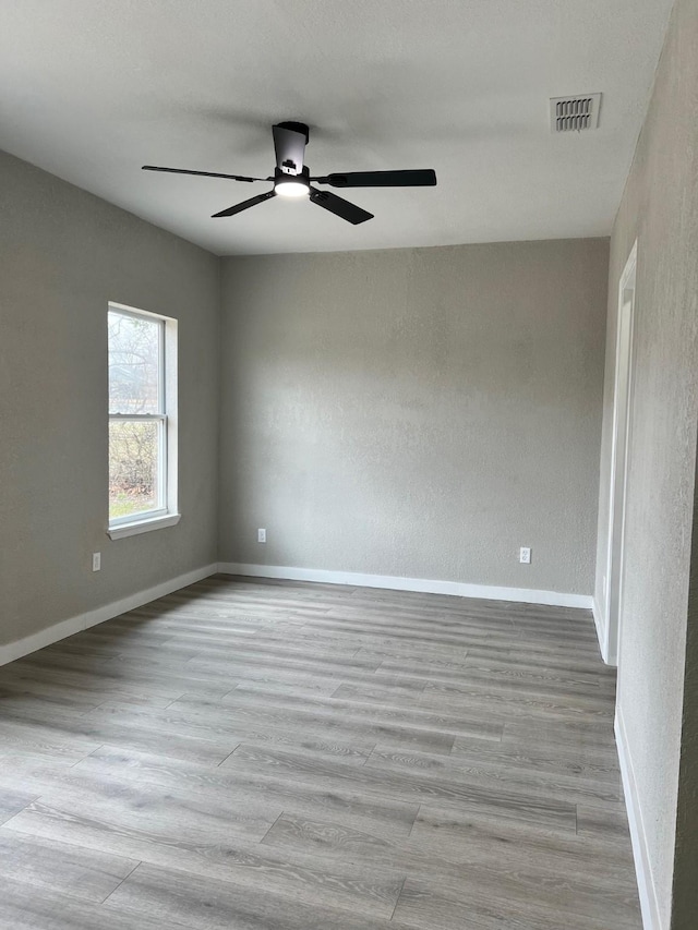 unfurnished room featuring ceiling fan, wood finished floors, visible vents, and baseboards