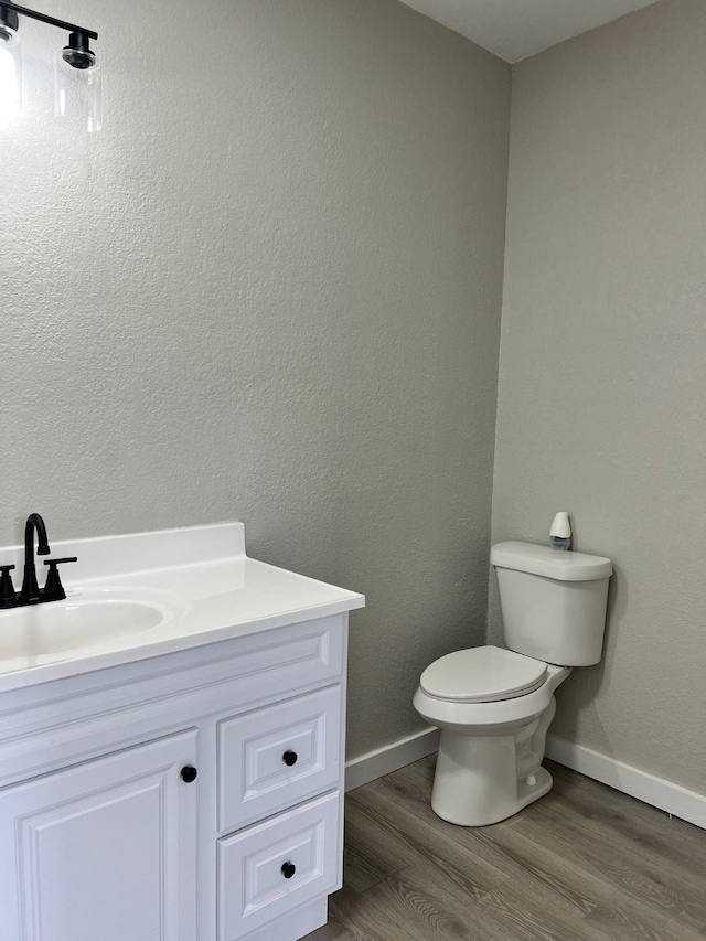 half bathroom with baseboards, a textured wall, toilet, wood finished floors, and vanity