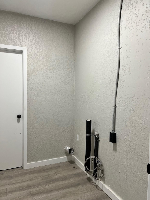 clothes washing area featuring baseboards, wood finished floors, and a textured wall