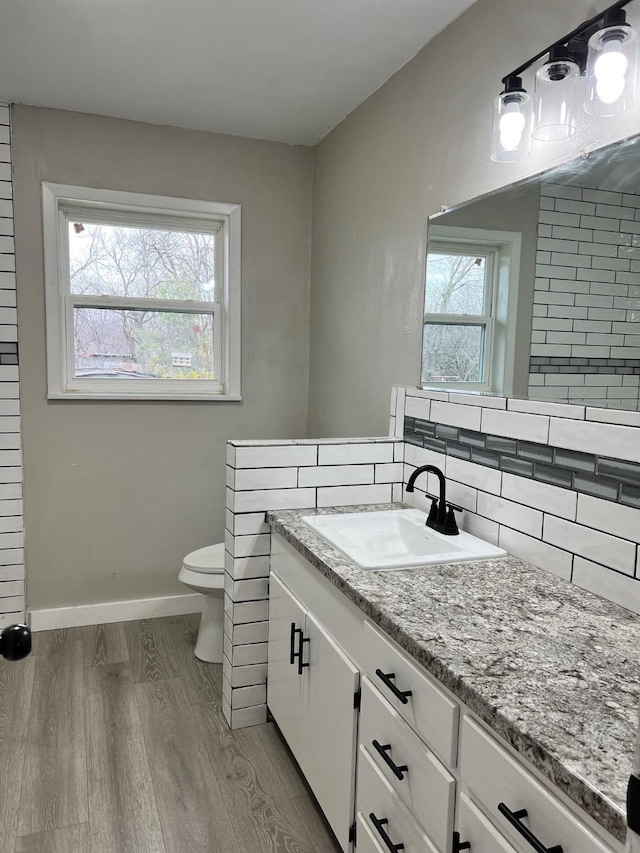 bathroom with a healthy amount of sunlight, toilet, backsplash, and wood finished floors