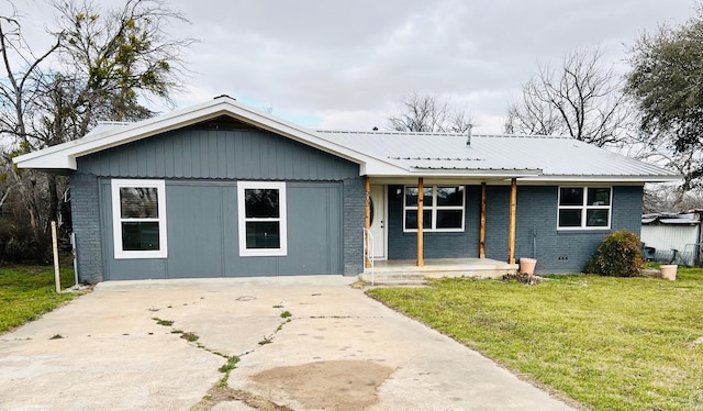 ranch-style house featuring metal roof, a porch, a front yard, and brick siding