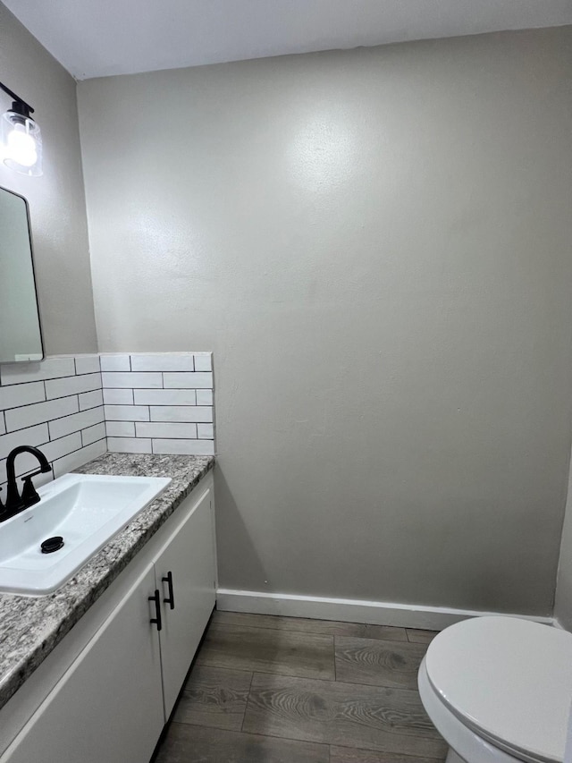 half bath featuring toilet, wood finished floors, vanity, baseboards, and decorative backsplash