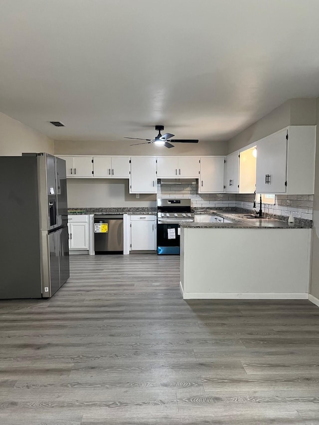 kitchen featuring stainless steel appliances, dark countertops, backsplash, and light wood-style floors