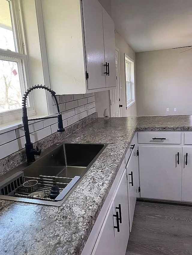 kitchen featuring a healthy amount of sunlight, white cabinets, backsplash, and a sink