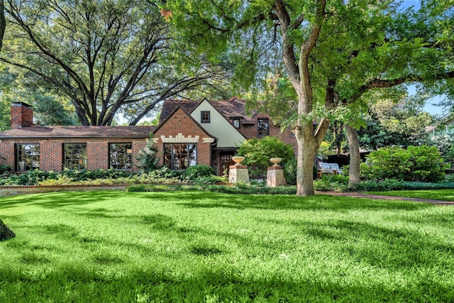 view of front of home featuring brick siding, a chimney, and a front yard