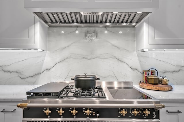 kitchen with tasteful backsplash, custom range hood, stainless steel gas stove, white cabinetry, and light stone countertops