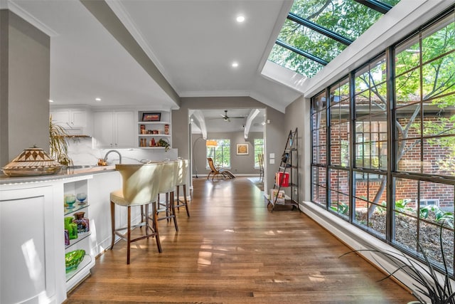 bar with a skylight, wood finished floors, a ceiling fan, ornamental molding, and tasteful backsplash