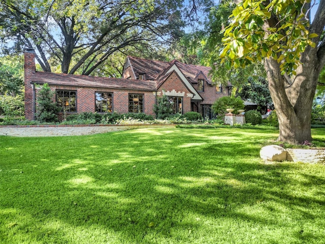 english style home featuring brick siding and a front yard