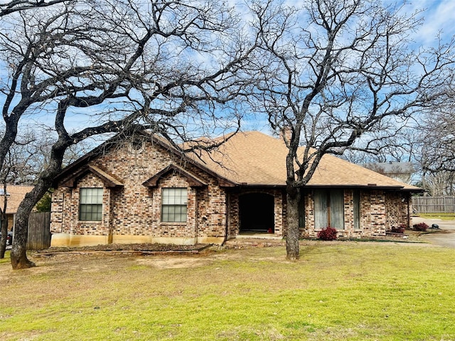 ranch-style house with a shingled roof, brick siding, fence, and a front lawn