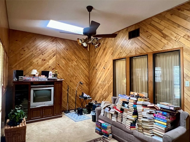 carpeted living room with ceiling fan, wood walls, and visible vents