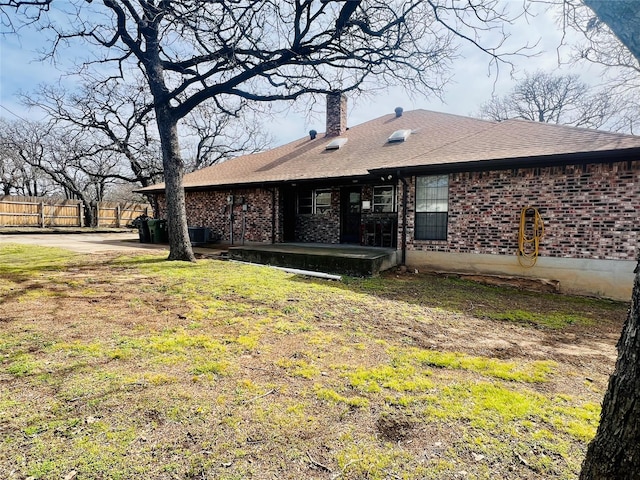 back of house with roof with shingles, a chimney, fence, and brick siding