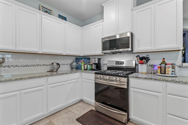 kitchen featuring tasteful backsplash, appliances with stainless steel finishes, light tile patterned flooring, white cabinetry, and light stone countertops