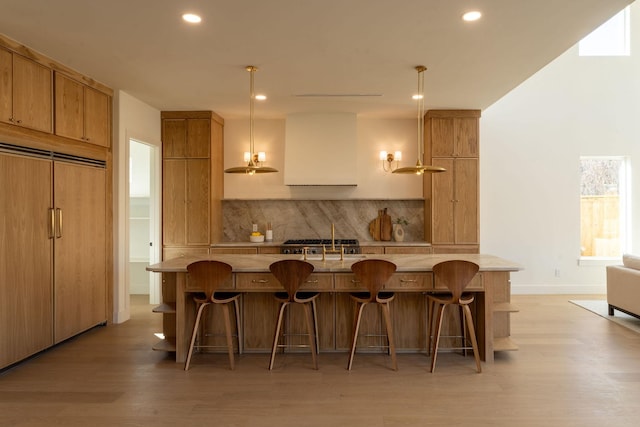 kitchen with tasteful backsplash, light wood-style flooring, paneled built in fridge, and a breakfast bar