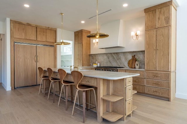 kitchen featuring a breakfast bar area, backsplash, a sink, light wood-type flooring, and premium range hood