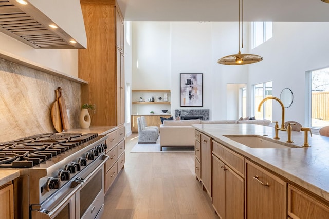 kitchen with a fireplace, light wood-style floors, a sink, wall chimney range hood, and double oven range