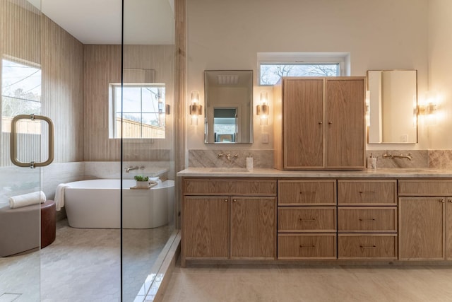 bathroom with double vanity, a wealth of natural light, a freestanding tub, and a sink