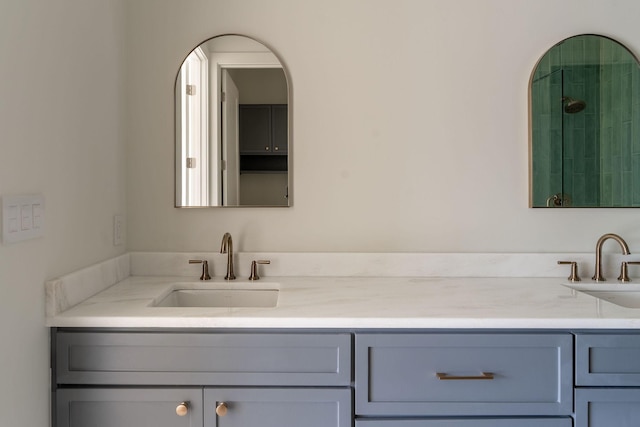 bathroom with tiled shower, a sink, and double vanity