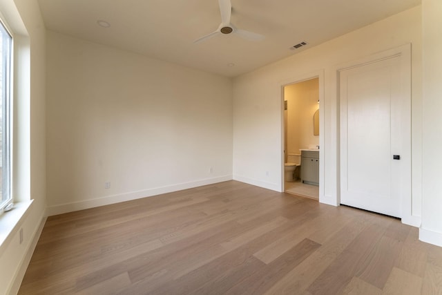 unfurnished bedroom with baseboards, visible vents, ensuite bath, ceiling fan, and light wood-style floors