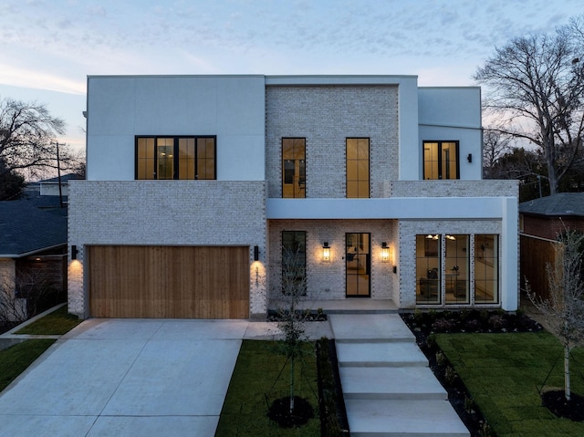 modern home featuring concrete driveway, brick siding, an attached garage, and a balcony