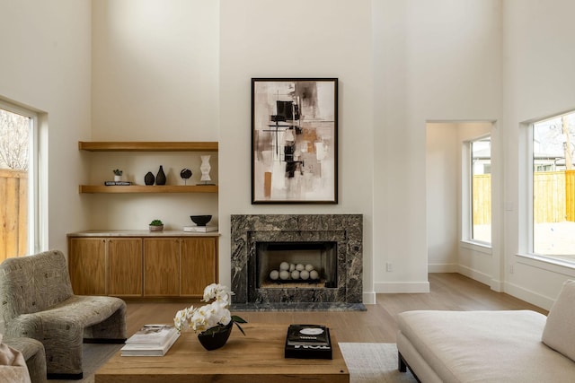 living area with light wood-style floors, a high ceiling, baseboards, and a premium fireplace