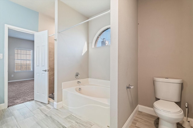 full bathroom featuring a garden tub, a shower stall, toilet, and baseboards