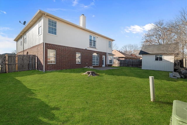 back of house featuring a fenced backyard, a chimney, a yard, an outdoor structure, and brick siding