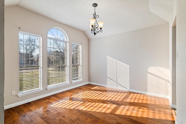 empty room with baseboards, vaulted ceiling, hardwood / wood-style floors, and a chandelier