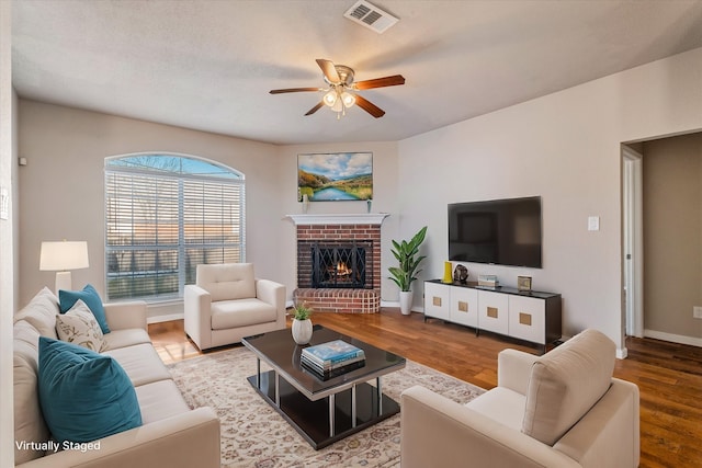 living room with a ceiling fan, a fireplace, visible vents, and wood finished floors