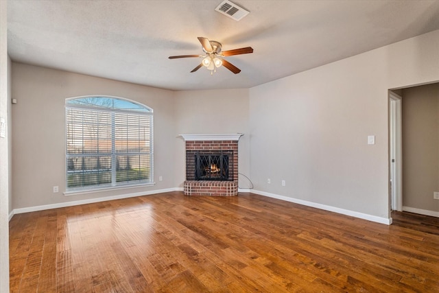 unfurnished living room featuring a brick fireplace, wood finished floors, visible vents, and baseboards