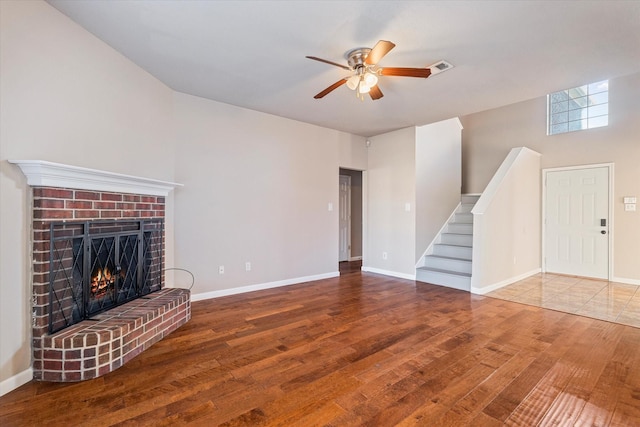 unfurnished living room featuring baseboards, hardwood / wood-style flooring, ceiling fan, stairs, and a brick fireplace