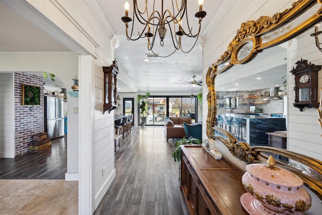 hallway with wooden walls, ornamental molding, wood finished floors, and a notable chandelier