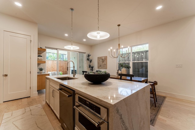 kitchen with light wood-style flooring, a kitchen island with sink, stainless steel oven, and a sink