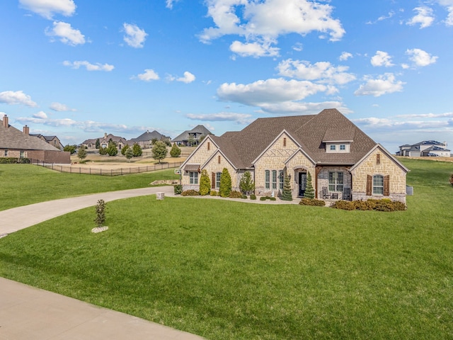 french provincial home featuring stone siding, a front yard, and fence